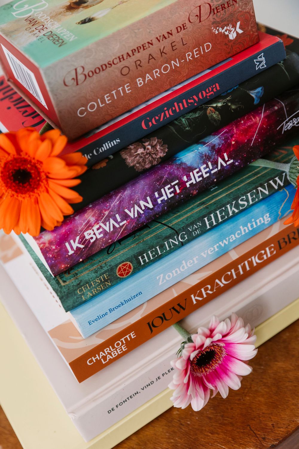 Stack of colorful books decorated with orange and pink gerbera daisies.
