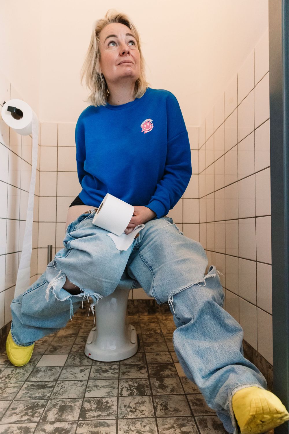 Bathroom photoshoot featuring blue sweater, jeans, and yellow socks on tiled floor.