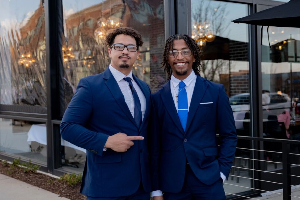 Group of men in navy blue suits and ties standing together outdoors.