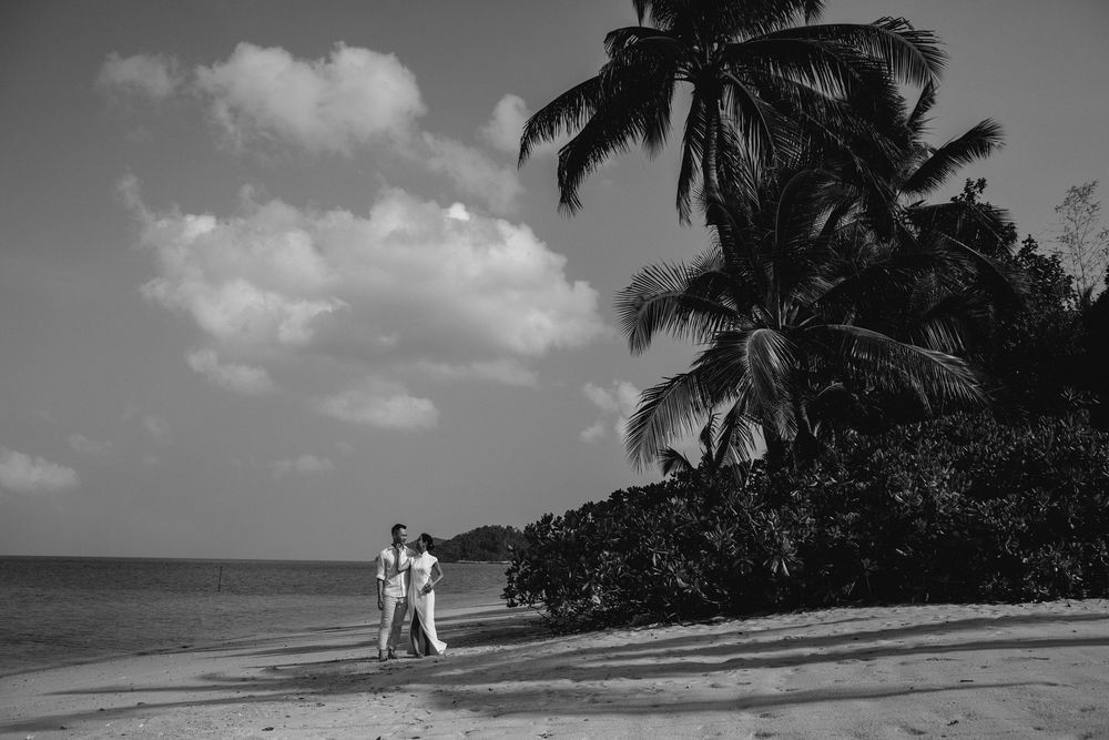 Bride and groom walk side by side along a serene, private Koh Samui beach, framed by palm trees and ocean views in a timeless black-n-white
