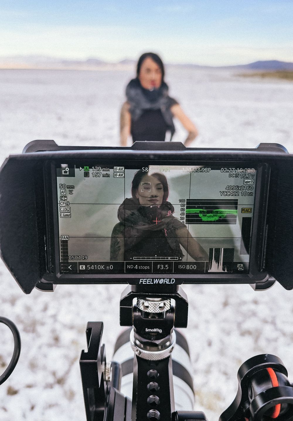 A woman being filmed outdoors on a salt flat, viewed through a Feelworld camera monitor in the foreground.