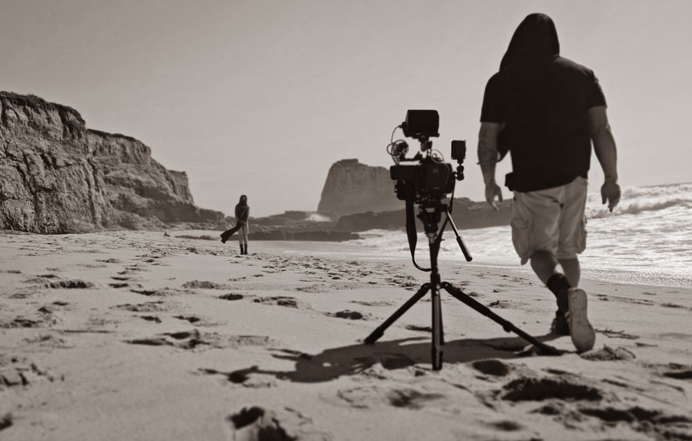 Black and white photographs of photographers setting up cameras on a sandy beach at sunset.