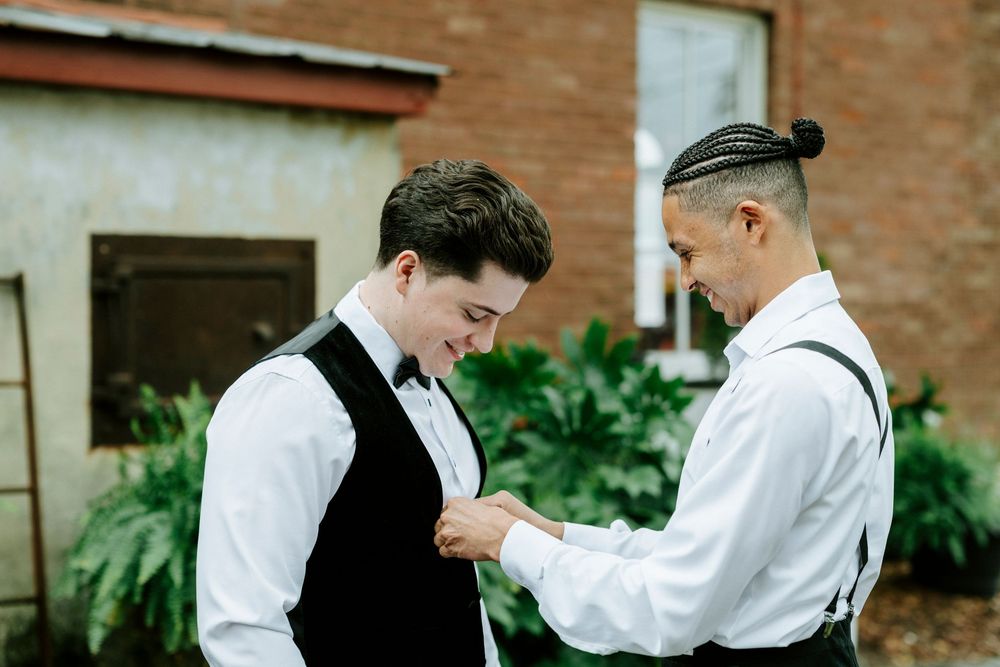 A group of groomsmen in formal attire prepare for a wedding ceremony while standing outdoors near a brick building.