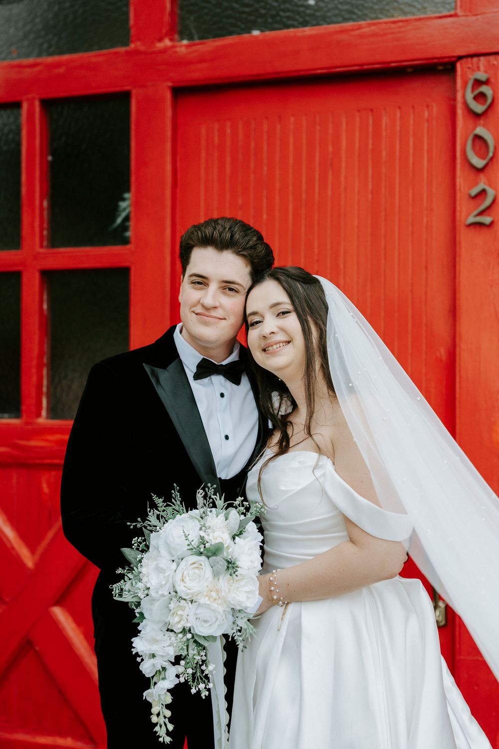 A series of romantic wedding portraits against bright red barn doors showing a couple with white flowers.