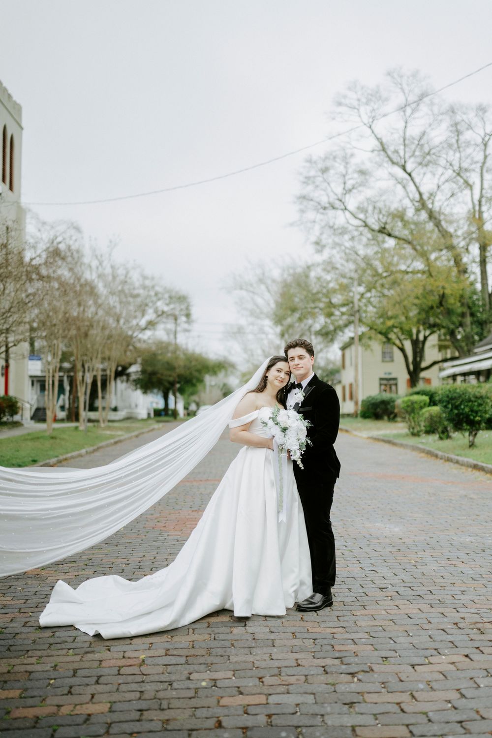 Wedding couple embraces on a brick paved street with flowing white dress and veil creating romantic composition.