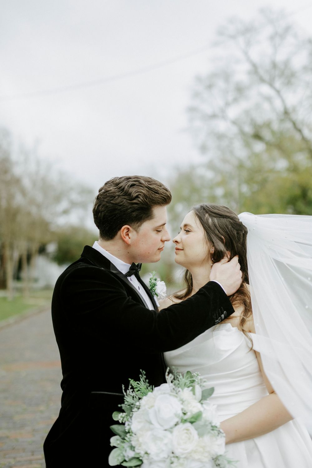 Romantic wedding portraits on a brick street showing tender moments between newlyweds with flowing white veil.