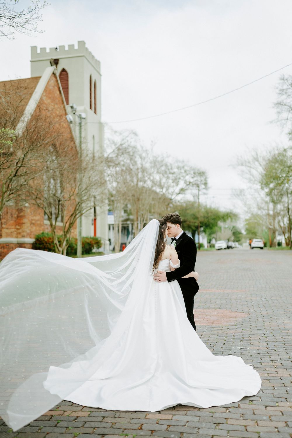 Dramatic wedding photos with flowing white dress and veil against historic church architecture and brick street.