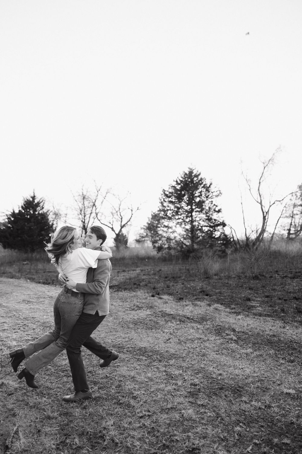 A joyful couple embraces and spins together in a natural outdoor setting captured in black and white.