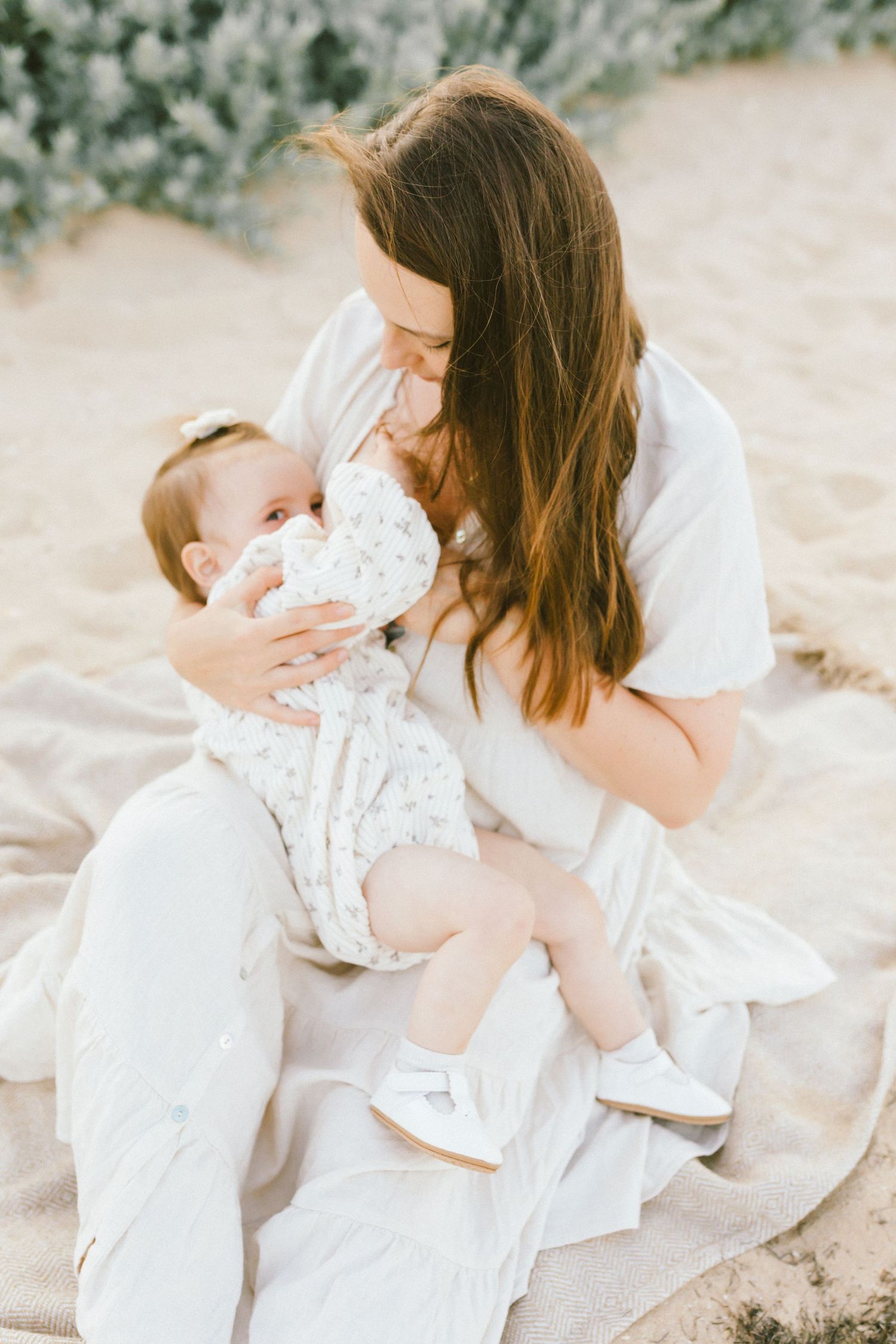 A tender moment captured in soft light as a mother in white embraces her baby wearing a floral print outfit.