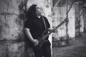 Black and white photo of a guitarist performing against a grungy concrete wall background.
