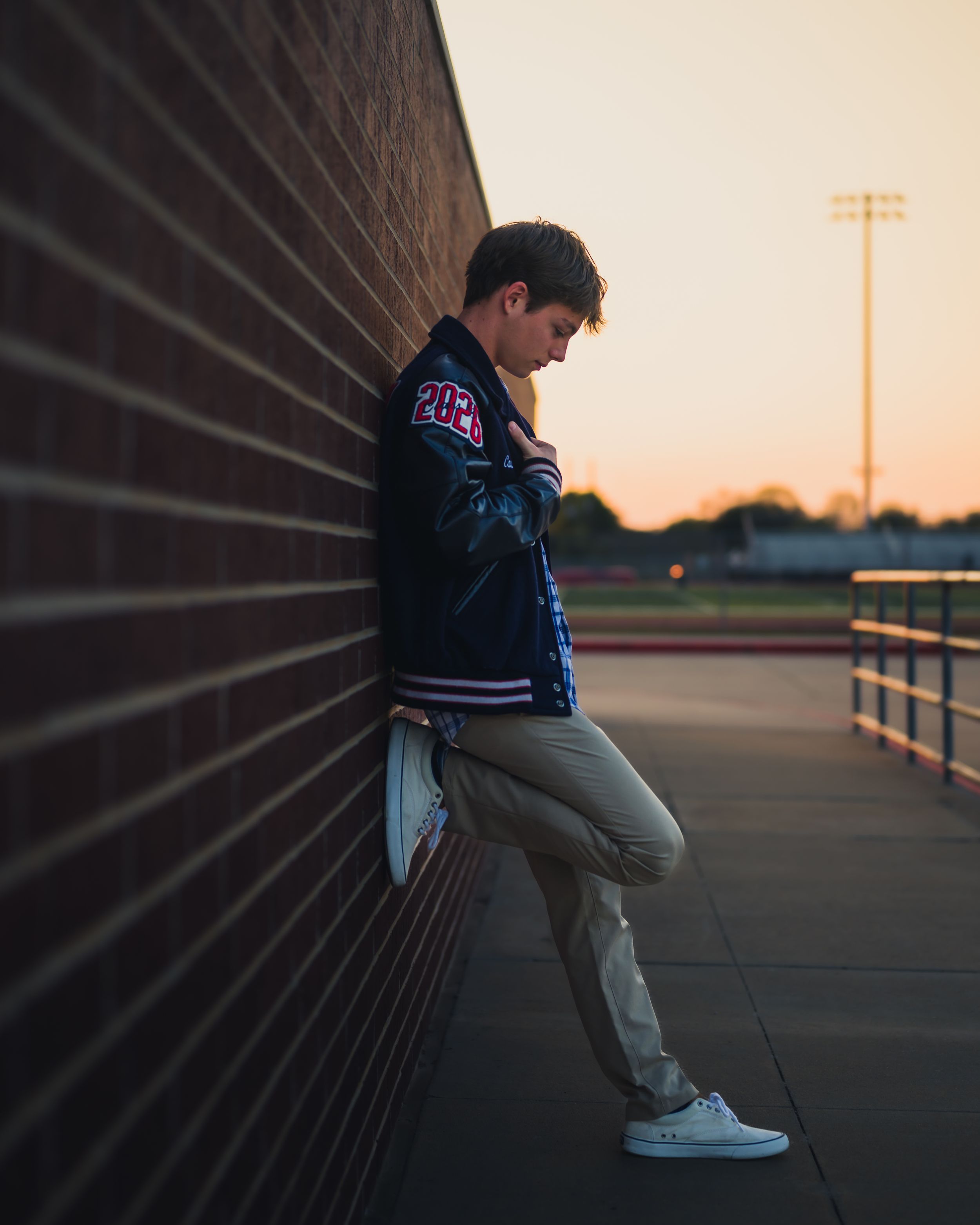 A person in casual wear sits on a bench against a geometric wall during sunset, creating a dramatic silhouette.