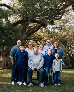 A family group poses together outdoors under large oak trees during a sunny autumn day.