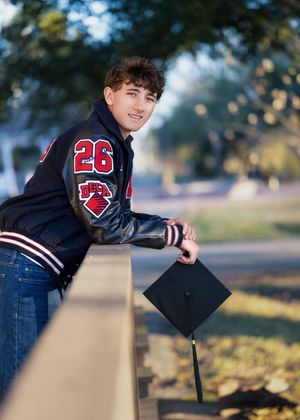 A graduate in a black gown holds their graduation cap while posing on railroad tracks during a photo session.