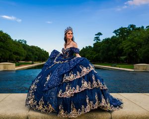 A flowing navy blue gown with intricate gold details spreads across a sandy beach near calm waters.