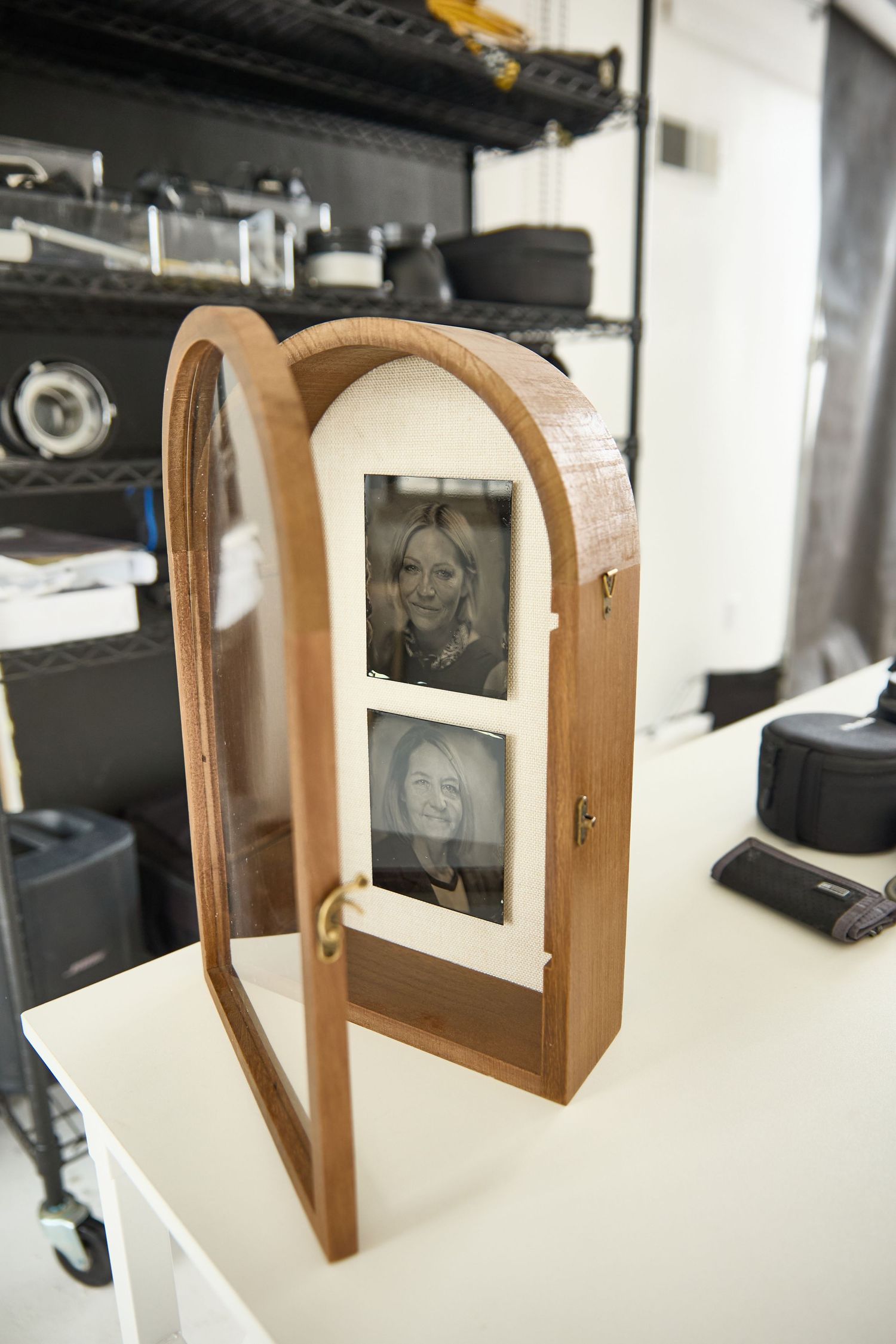 A wooden arched photo frame holder displays two vintage black and white photographs on a white surface.