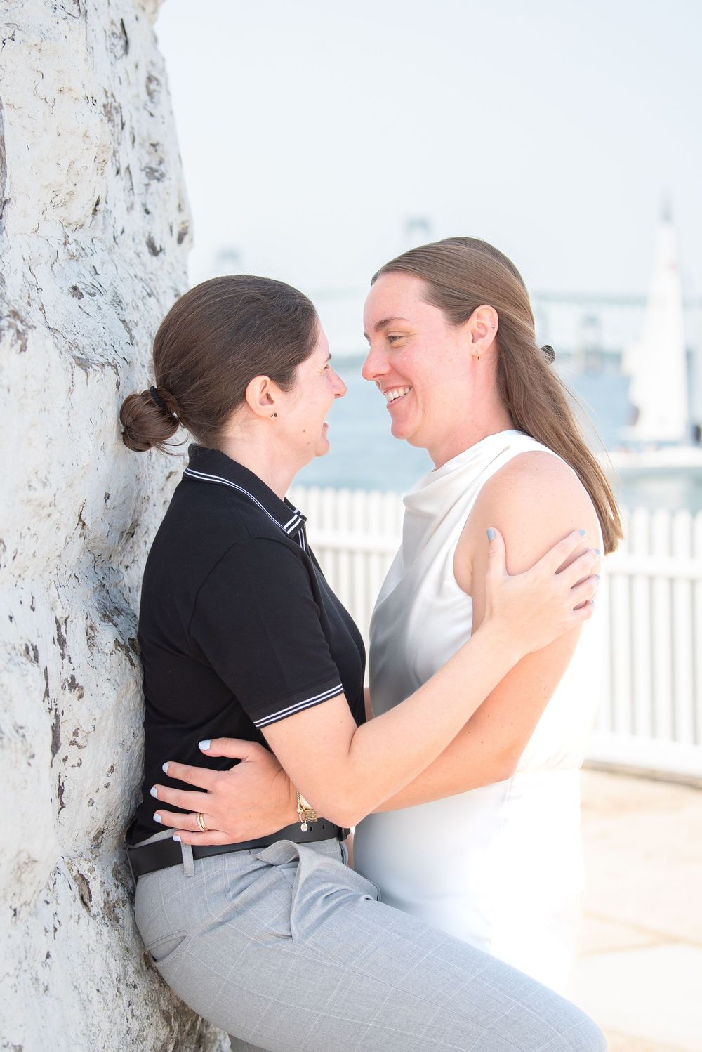 A tender moment between a couple leaning against a stone wall during a seaside photoshoot.