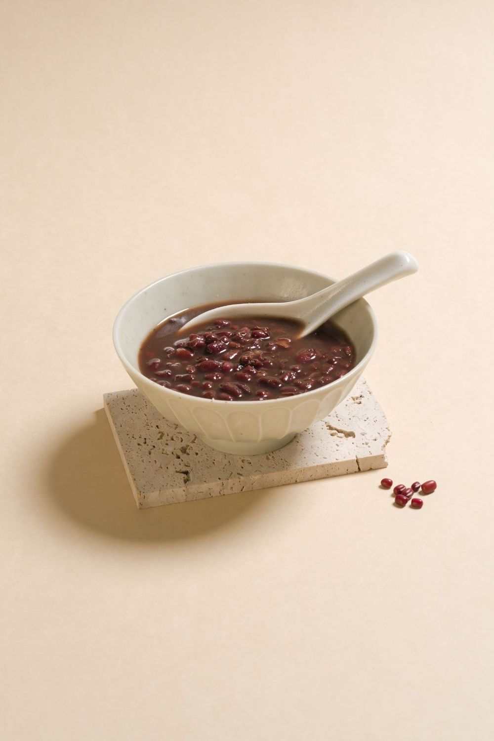 A series of white ceramic bowls containing red bean dessert shown in a minimalist composition.