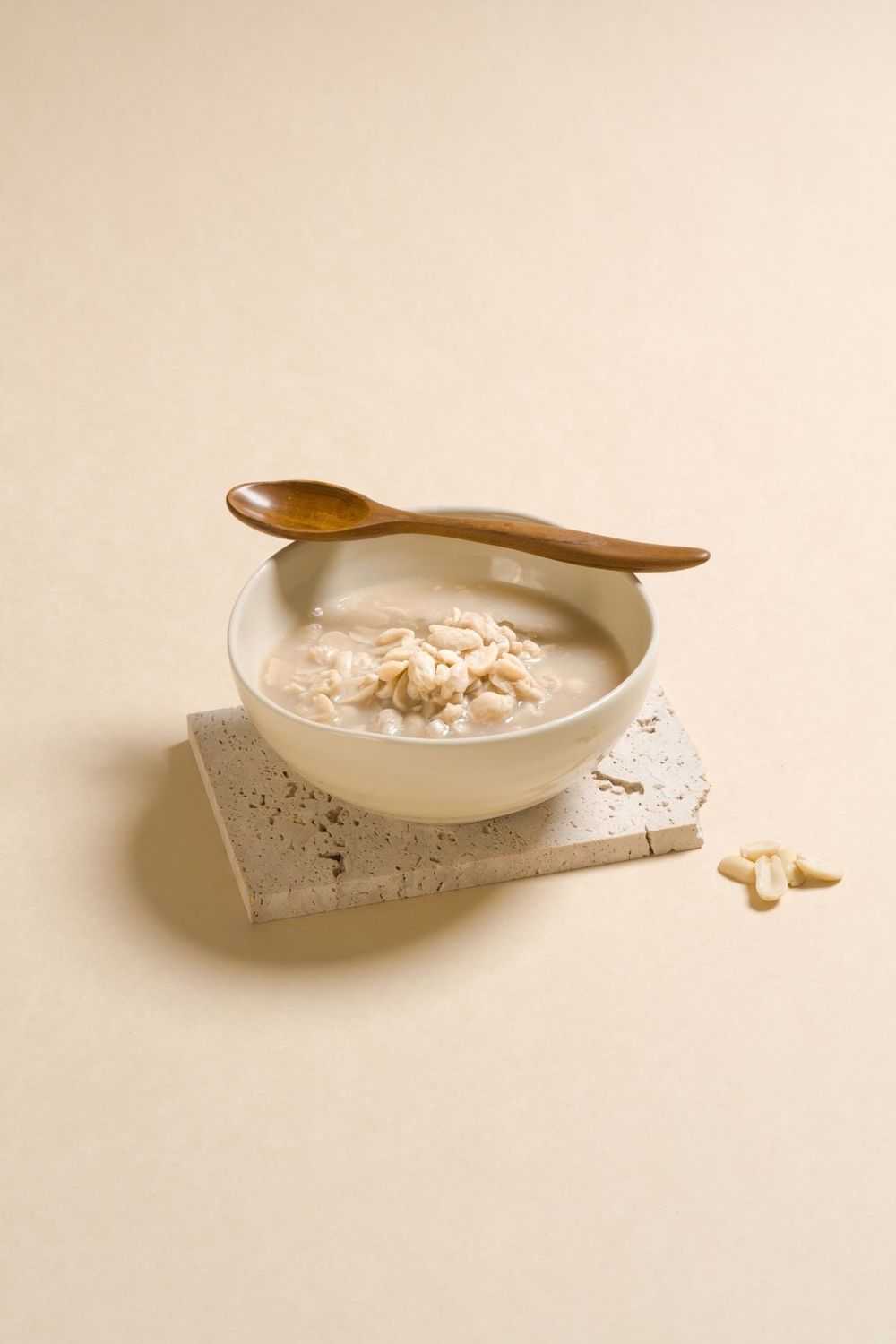 White ceramic bowl with creamy sauce and wooden spoon on neutral background in minimalist style.