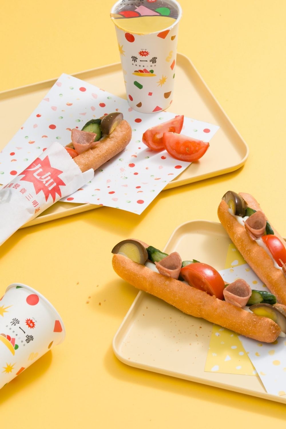 Fresh submarine sandwich with tomatoes and cucumbers served on white paper against yellow background.