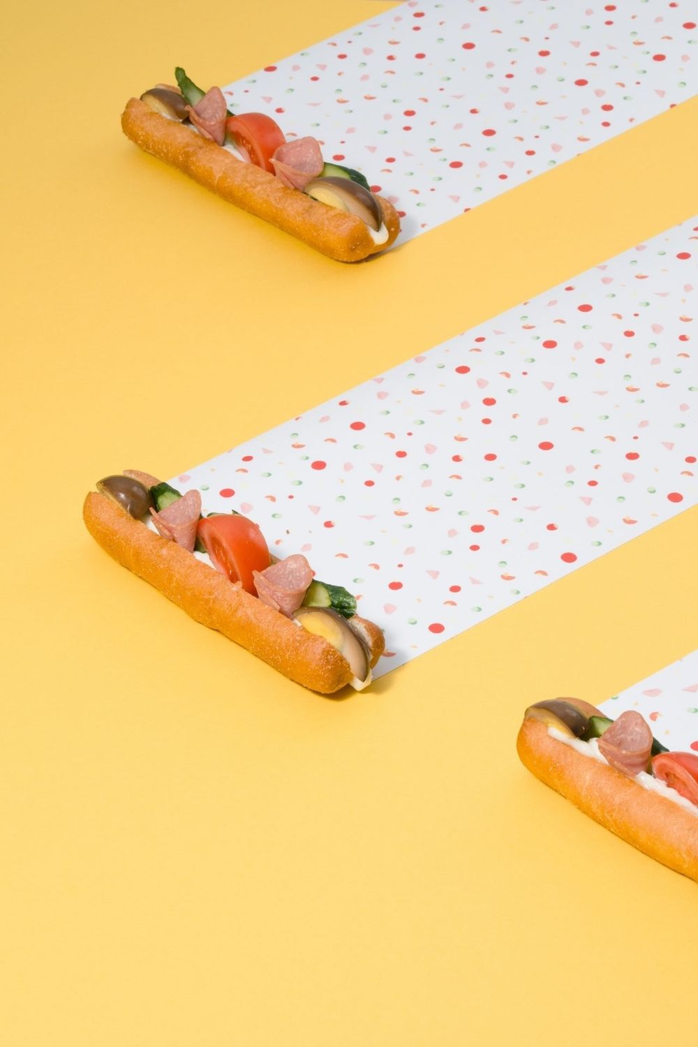 Row of hot dogs arranged diagonally on polka dot pattern against yellow background.