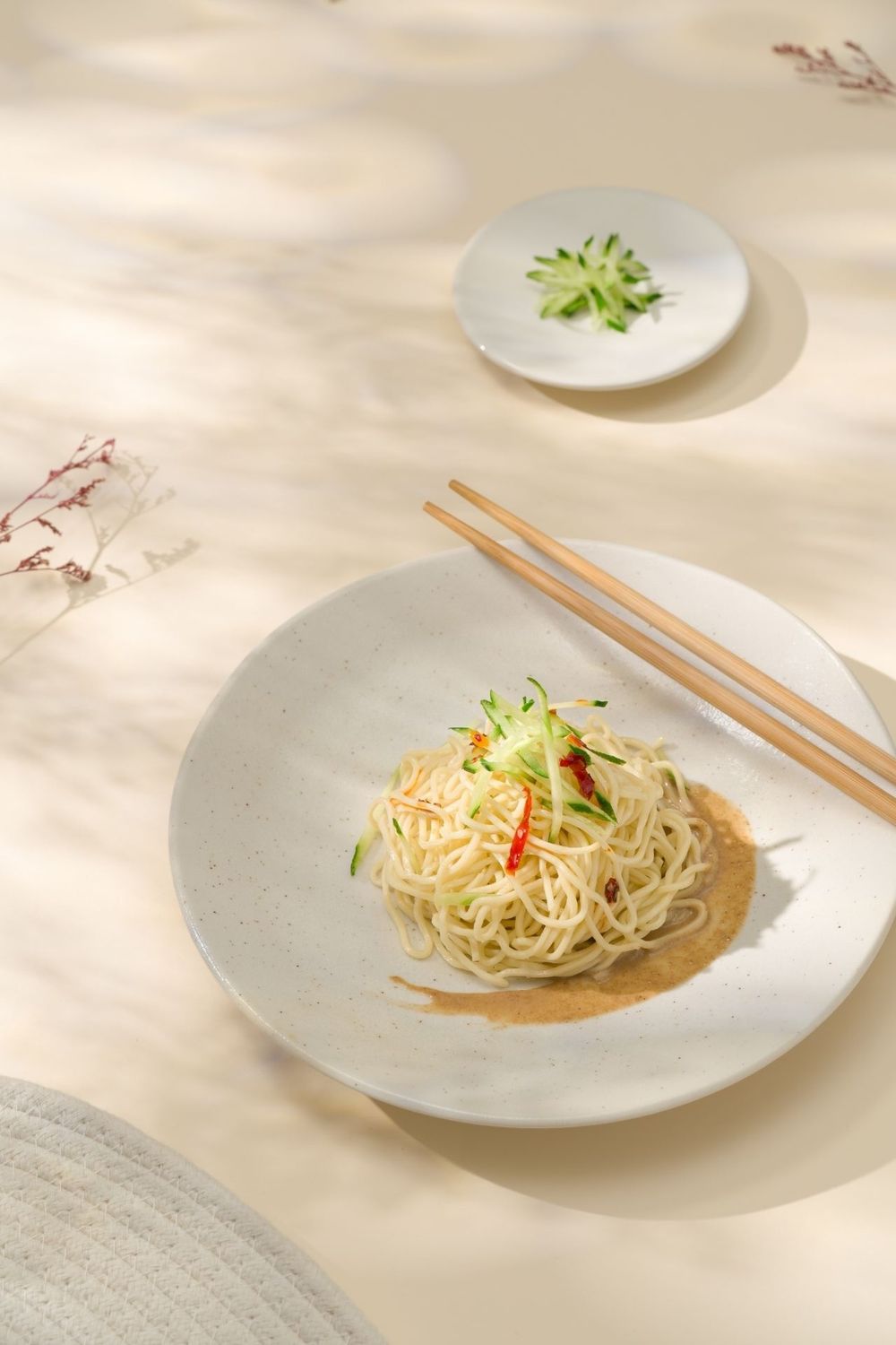 A series of minimalist plated noodle dishes with garnishes on white ceramic plates against a light background.