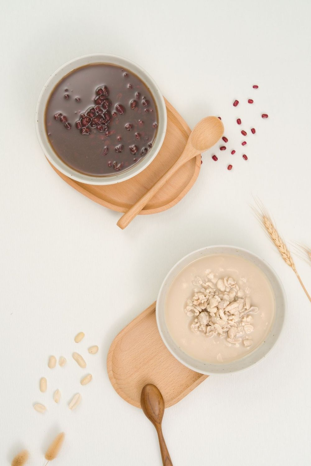 Wooden spoons and small bowls containing chocolate and cream-colored sauces on white surface.