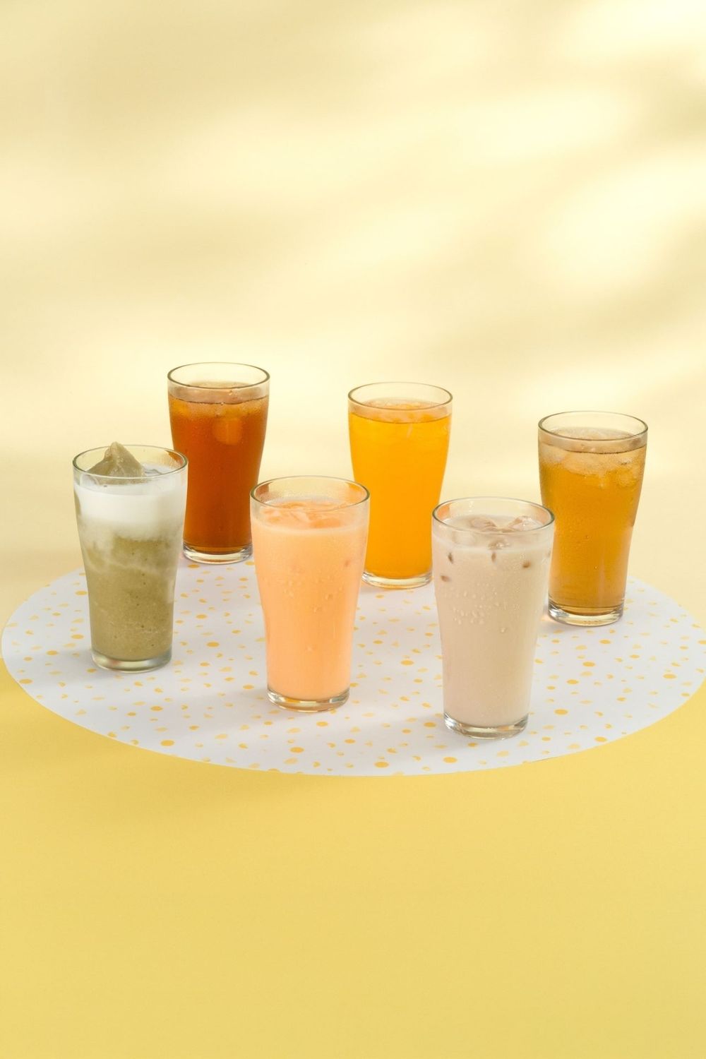 Collection of colorful smoothies and beverages in small glasses arranged on polka dot surface.
