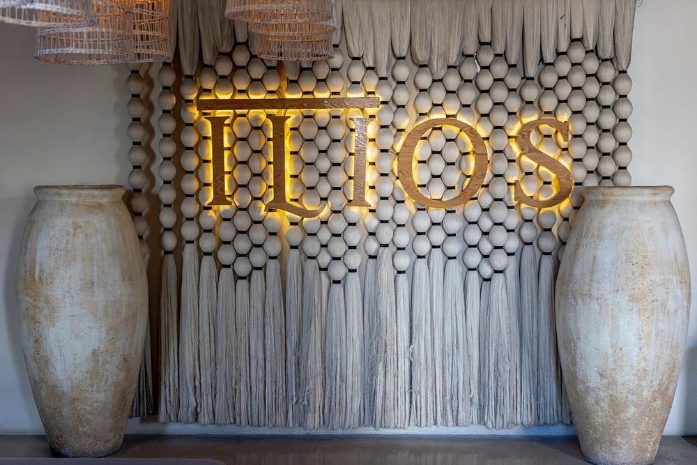 Large ceramic urns flank a decorative wall with hanging macrame and a neon sign in an elegant restaurant setting.