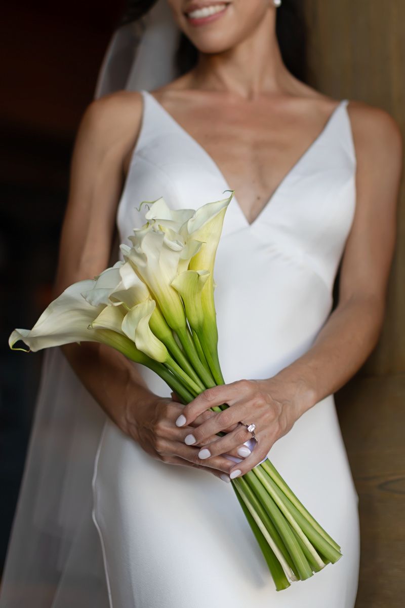 Elegant white calla lily bouquet held by a bride in a classic white wedding dress.