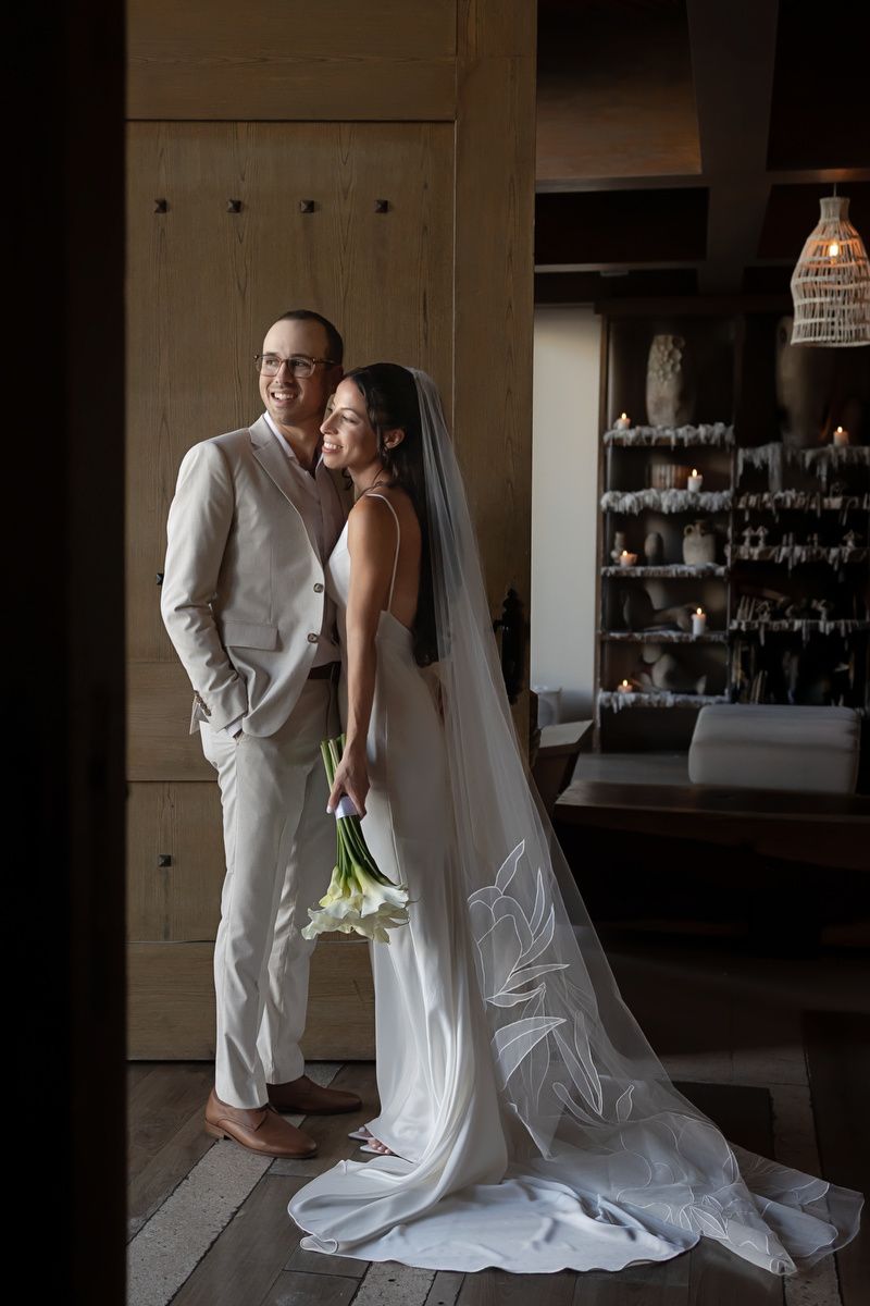 Romantic wedding couple in white attire share an intimate moment in moody lighting.