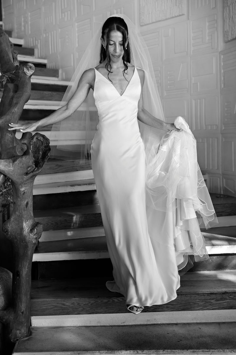Black and white photo of a bride ascending stairs in an elegant white gown.