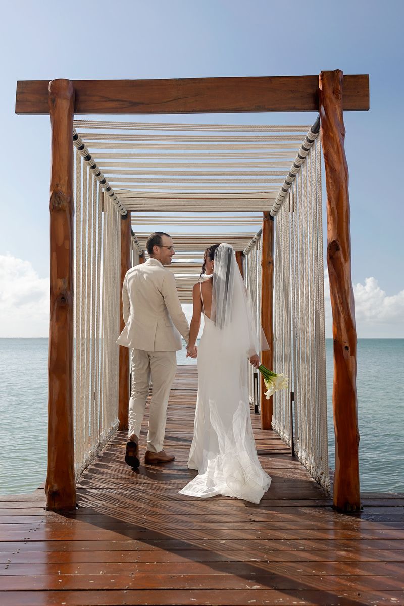 A couple in wedding attire stands on a wooden pier overlooking the ocean in a series of romantic photos.