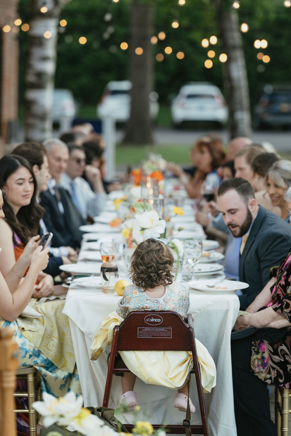 Long banquet tables set with white linens and floral centerpieces for an outdoor evening reception.