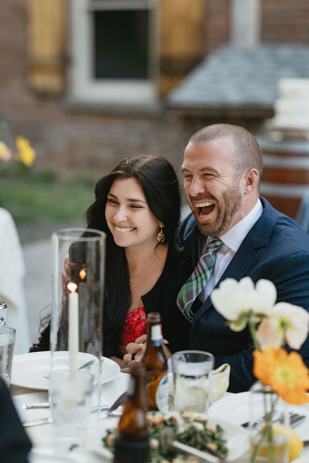 People enjoying laughter and conversation at an elegant dinner party with table settings and floral decorations.