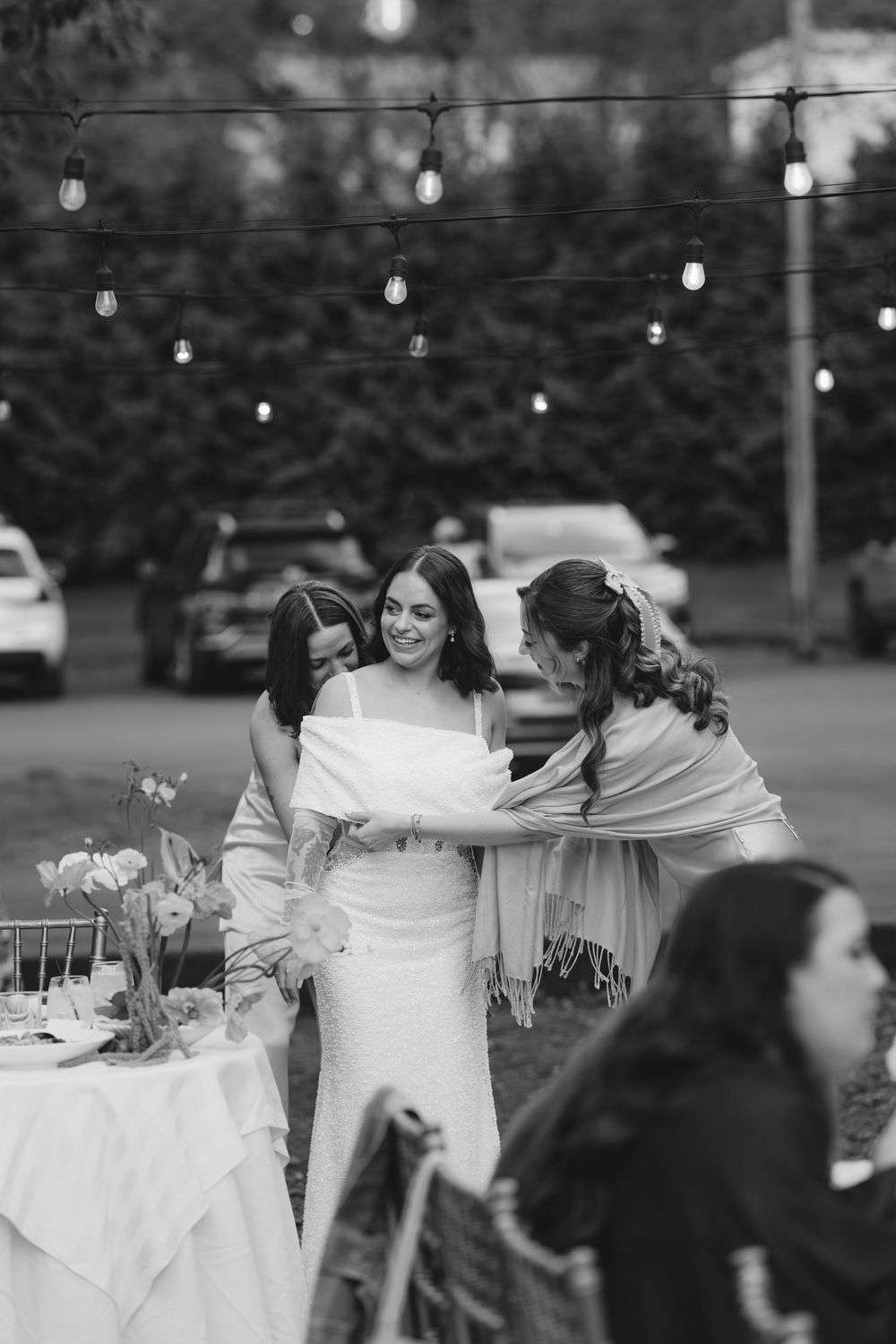 Black and white photo of an outdoor evening reception with string lights and elegant table settings.