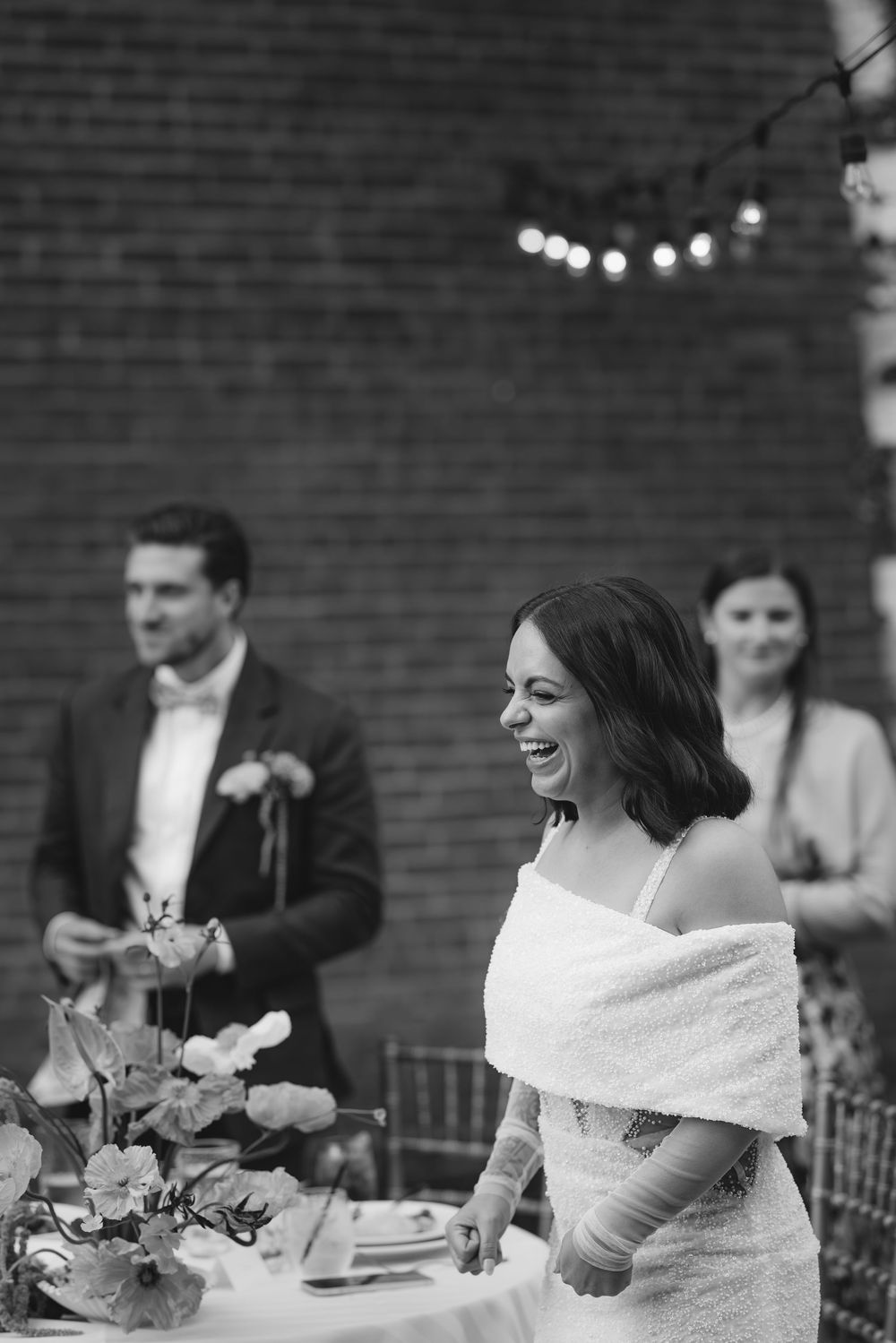 Wedding reception tables decorated with elegant floral arrangements and white linens against exposed brick walls.