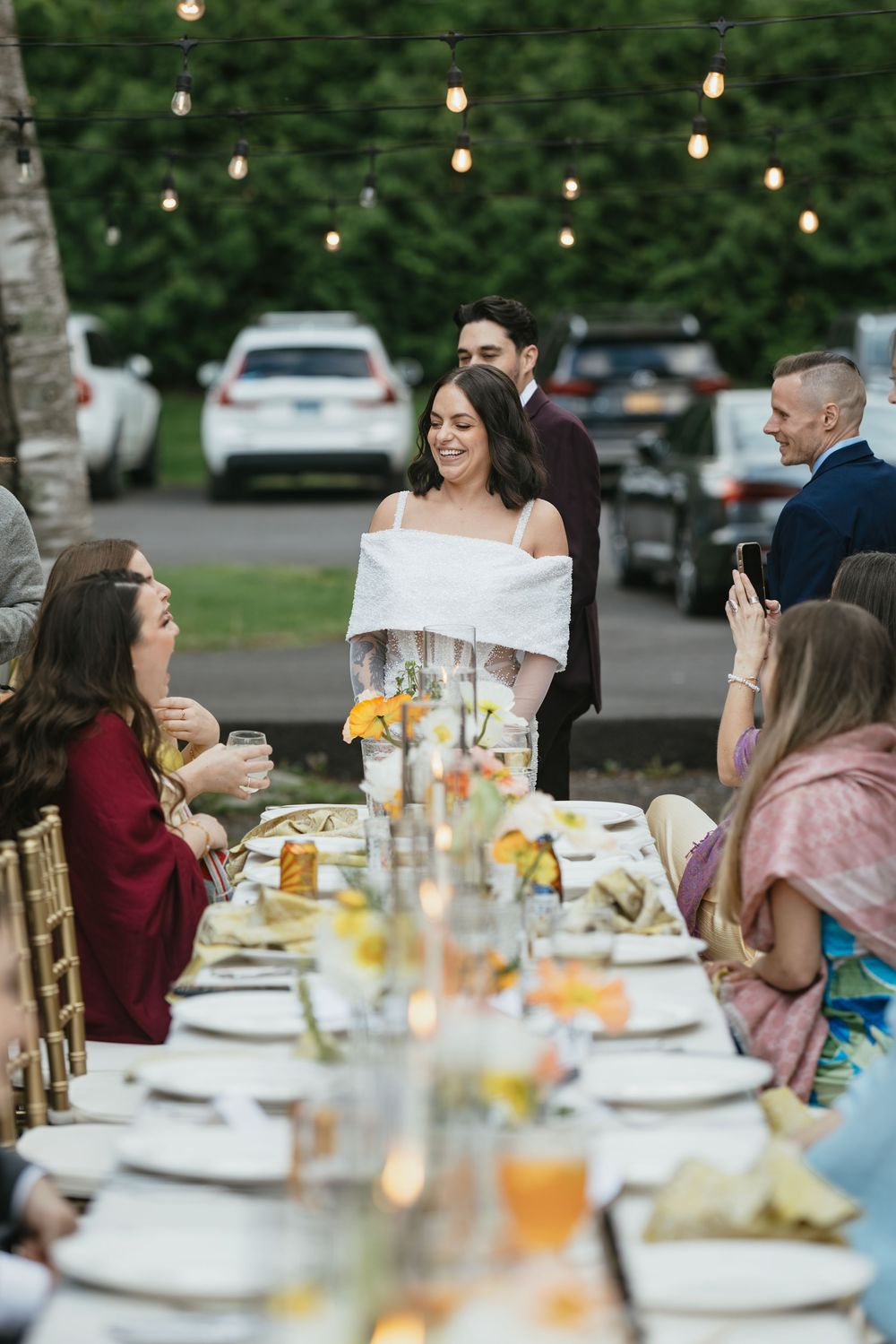 Wedding reception dinner table set with glassware and centerpieces under outdoor string lights.