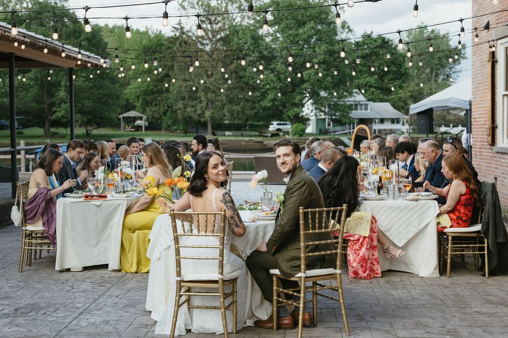 Guests enjoy an elegant outdoor reception dinner at dusk with string lights overhead and tables set with white linens.