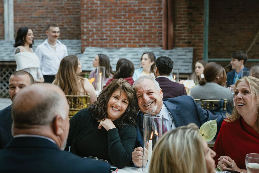 A lively gathering of people socializing and laughing together at an indoor event with brick walls.