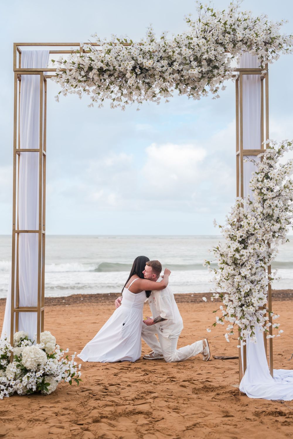 Couple standing under floral arch during beach engagement session at Wyndham Grand Rio Mar
