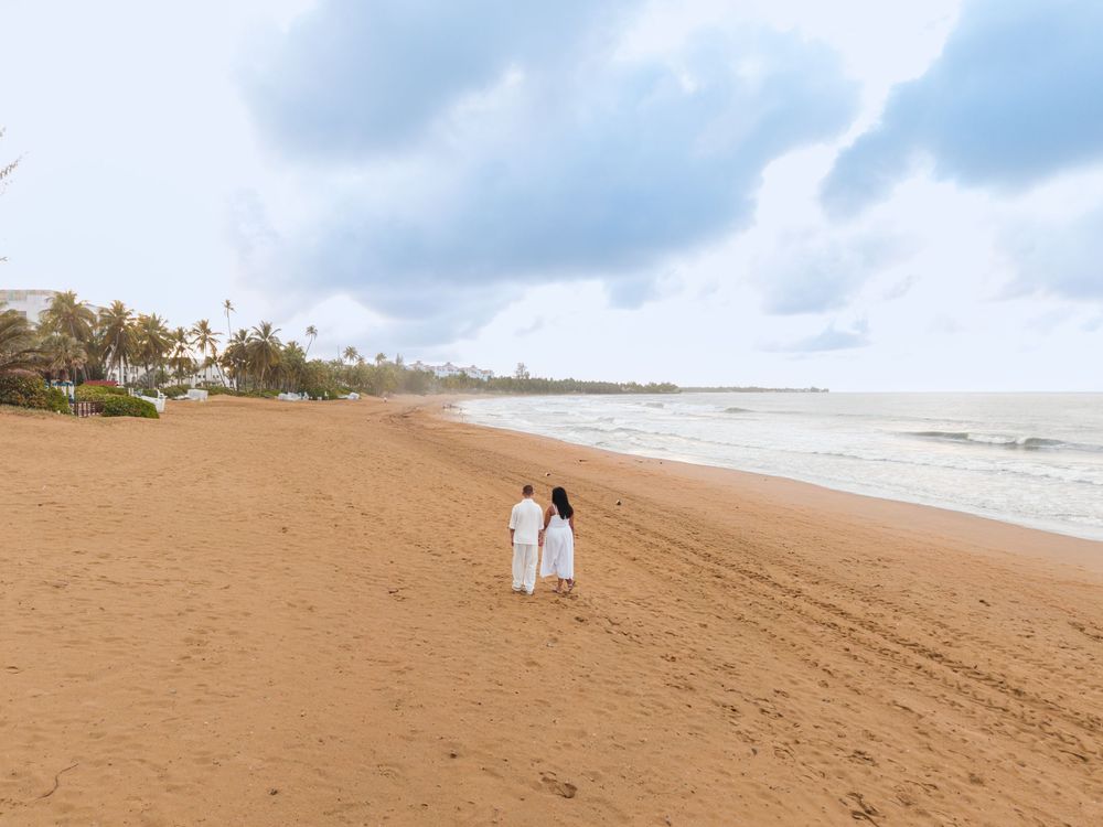 Wide view of couple walking on beach during engagement session at Wyndham Grand Rio Mar in Puerto Rico