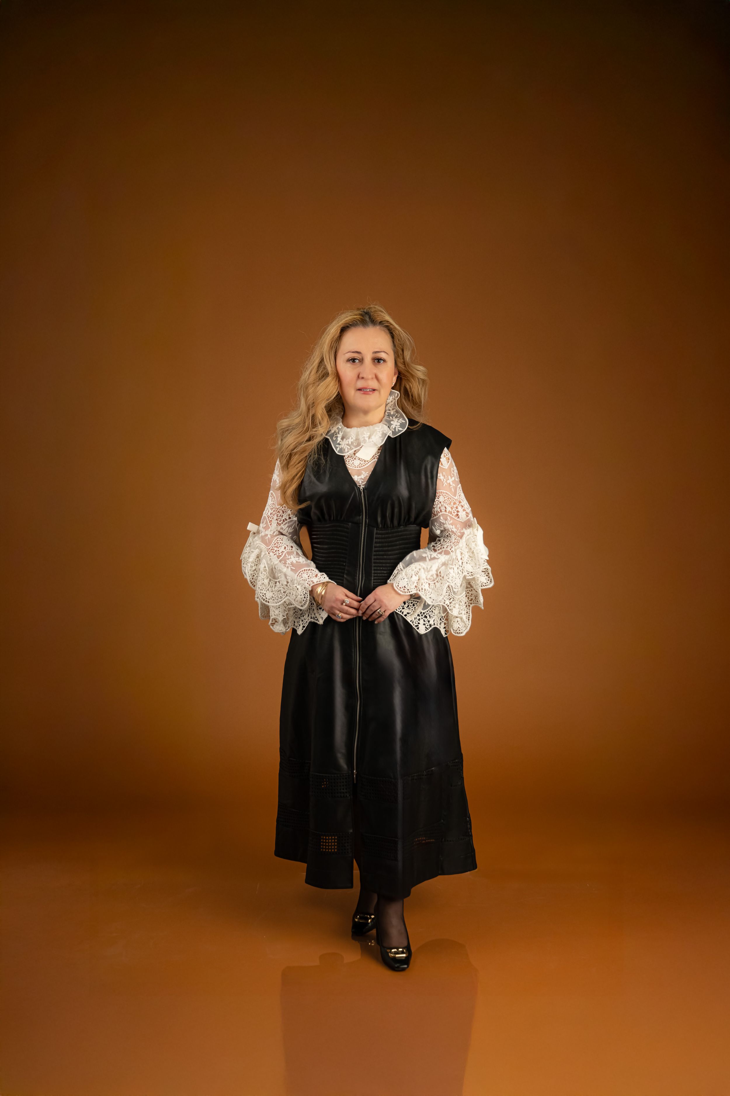 High-fashion glamour portrait of a woman in a black leather dress over a crisp white shirt, posed in a studio with soft lighting and a sophi