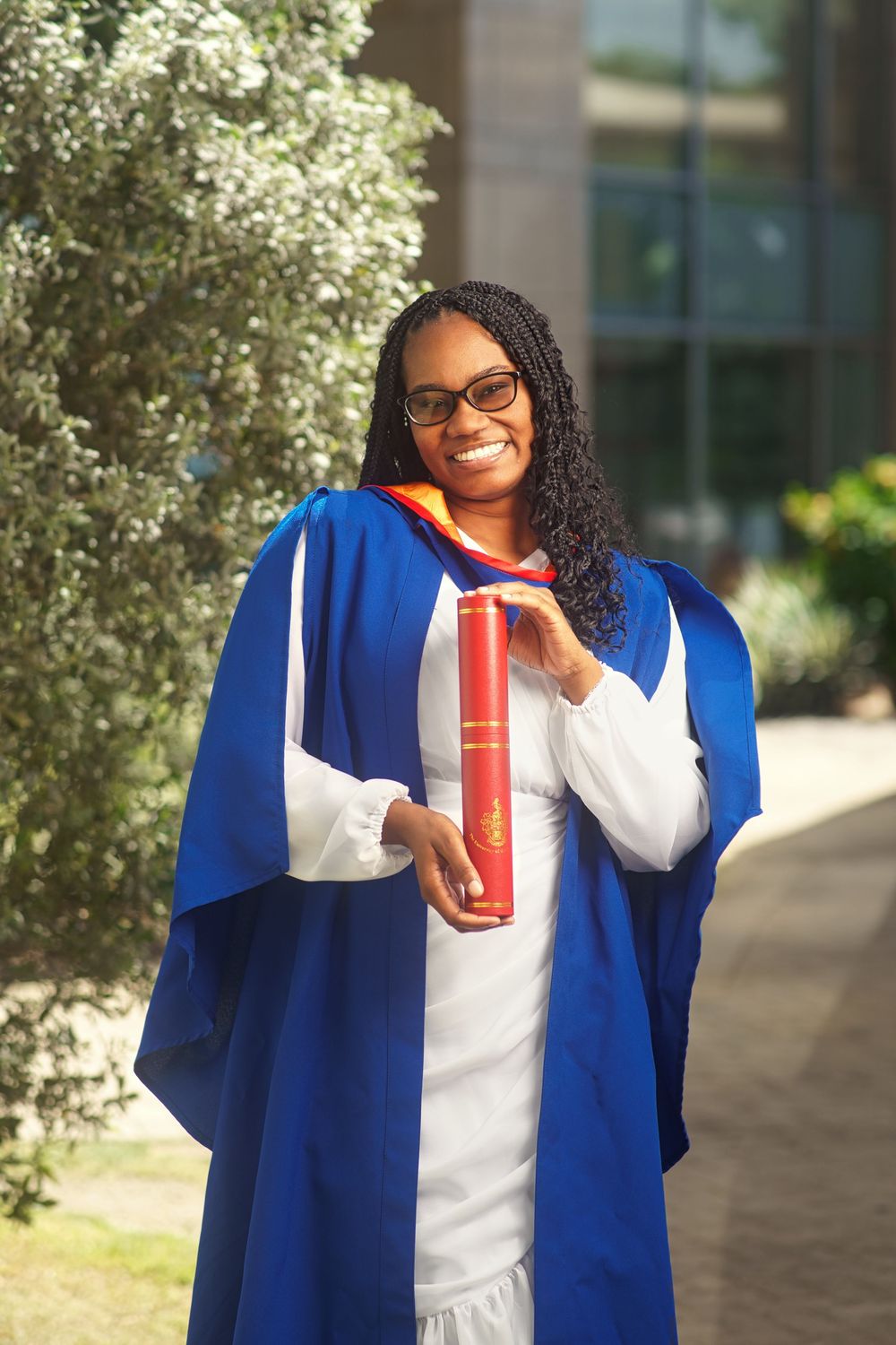 Graduate in blue academic regalia smiles while holding a red drink cup in outdoor setting.