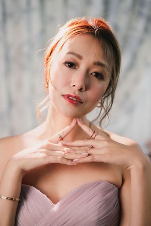 Young Asian woman in strapless pink dress with hands clasped near chin in elegant portrait.