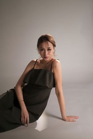 Woman in olive green slip dress sitting gracefully on floor, posing for fashion portrait against neutral gray background.