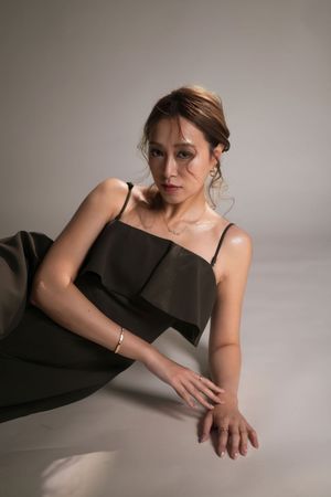 Woman in elegant dark olive spaghetti strap dress posing gracefully on floor, wearing gold jewelry, studio portrait.