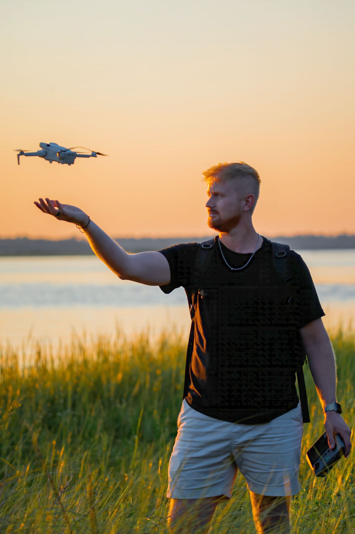 A Wilmington Photographer flies near an outstretched hand against a golden hour sunset sky over water in Carolina Beach State Park.
