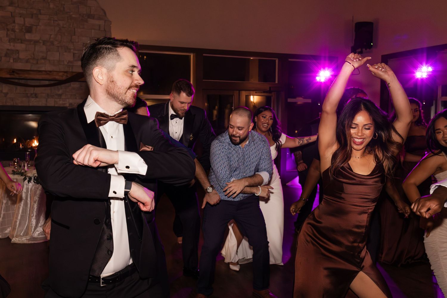 People dancing and celebrating at a wedding reception with purple lighting and festive atmosphere.