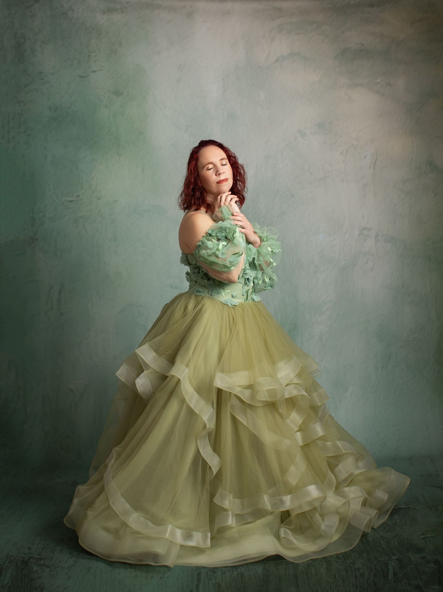 Ethereal portrait in flowing sage green ball gown against moody dark background.