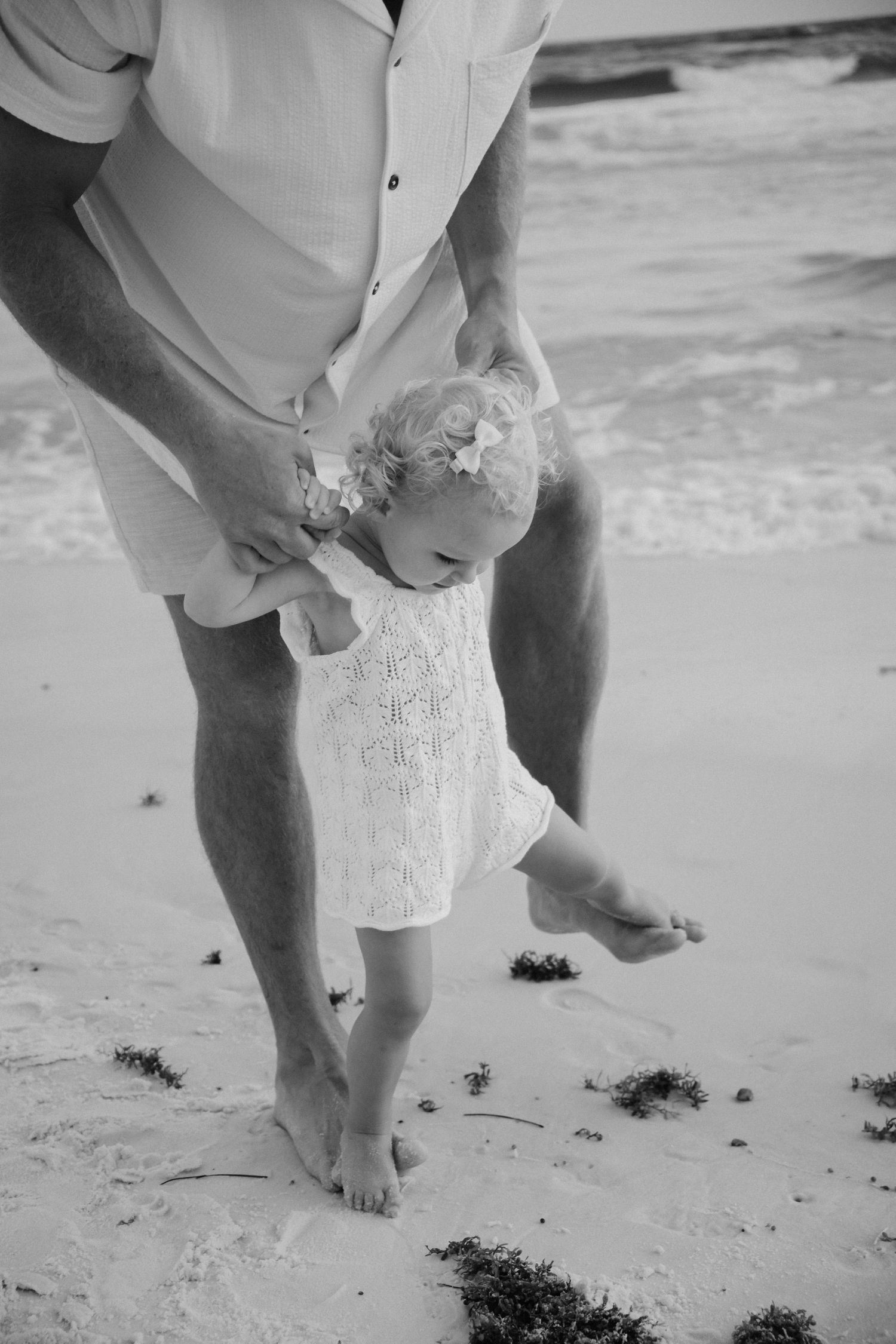 Baby in sunhat playing with seashell in sand on beach.
